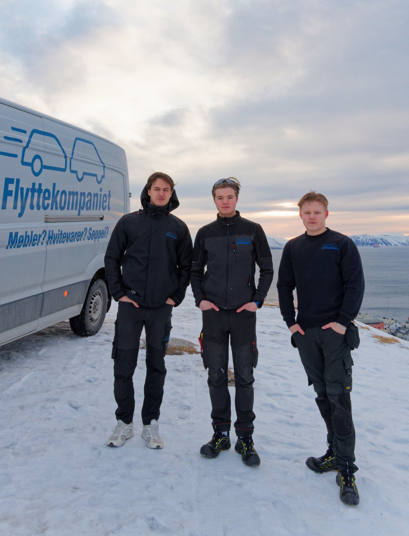 Tre av Flyttekompaniets ansatte foran firmabilen med slagordet «Møbler? Hvitevarer? Søppel?»